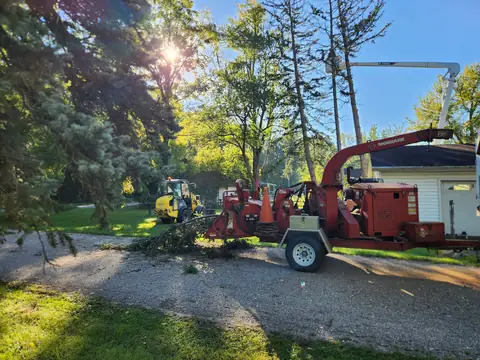 Red tow-behind chipper parked on a gravel drive during cleanup
