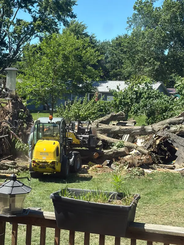 Compact loader carrying cut logs across a backyard past a deck