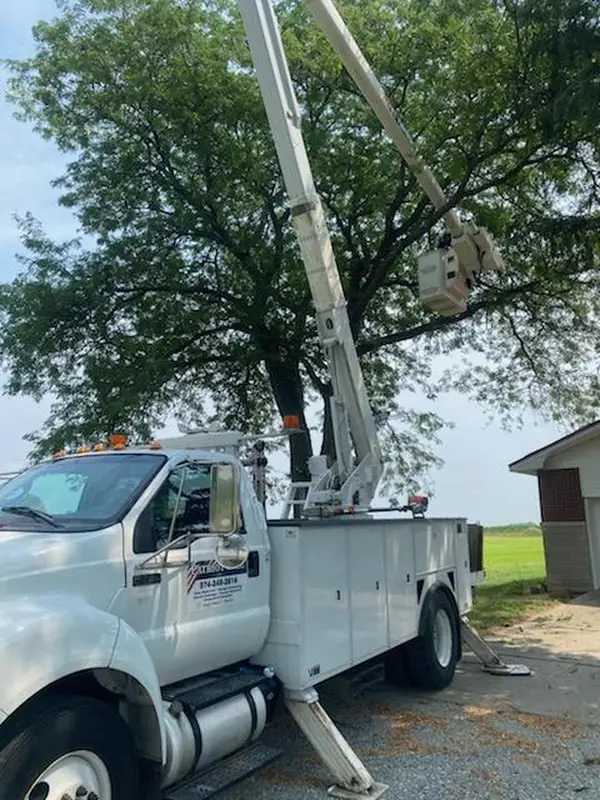 Patriot Tree Corp bucket truck with the company logo on the door, boom raised into a tree