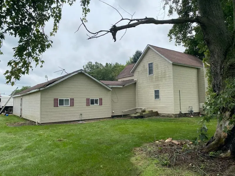 After: the same two-story farmhouse with the storm tree removed and the lawn cleared